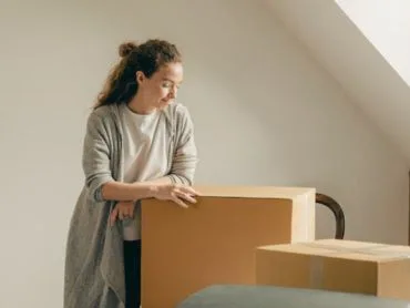 Pourquoi je n’arrive pas à me mettre à désencombrer ma maison ? une femme blonde réfléchi en regardant des cartons d’emballage