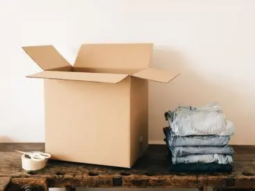 Les éléments pour commencer à trier son lieu de vie La photo d’un carton ouvert avec du scotch et des ciseaux à côté d’une pile de quatre jeans