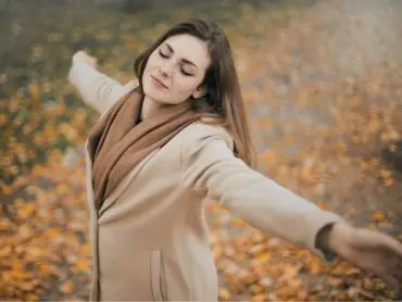 La photo d’une femme portant un manteau beige ouvrant les bras avec un visage épanoui illustrant le passage à l’action dans le désencombrement de sa maison