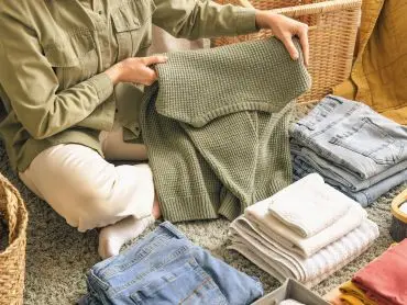 La photo d’une femme assise sur un tapis qui est en train de plier du linge et de faire des piles pour une gestion du linge efficace grâce au home organising et au home management